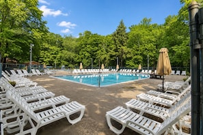A swimming pool with white lounge chairs and umbrellas, surrounded by trees.