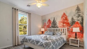 Un dormitorio con cama, mesita de noche, ventilador de techo y ventana con cortinas.
