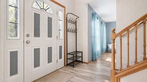 Un pasillo con una escalera de madera, un perchero y una puerta con paneles de vidrio esmerilado.