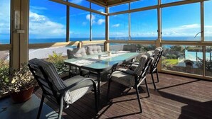 A covered outdoor patio with a glass table and chairs, overlooking a scenic view. - Ocean View Holiday Home near Beach in Mount Martha (Mount Martha)