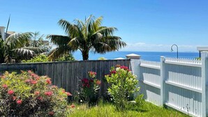 A coastal view with a wooden fence, palm trees, and flowering plants. - Ocean View Holiday Home near Beach in Mount Martha (Mount Martha)