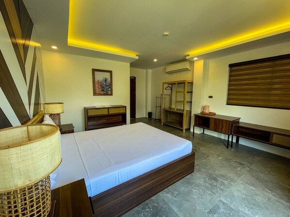 A modern hotel room with a large bed, wooden headboard, bedside tables, a wardrobe, and a small seating area with a table and chairs. - Red Picnic Hostel (Panglao)