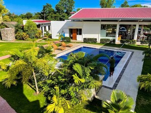 A residential property with a swimming pool surrounded by lush greenery and a red-roofed house. - Red Picnic Hostel (Panglao)