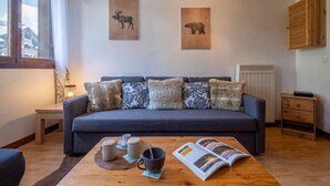 Un salon comprenant un canapé, une table basse avec des tasses et un magazine, une lampe, et deux reproductions d’œuvres d’art représentant des animaux, encadrées et accrochées au mur.