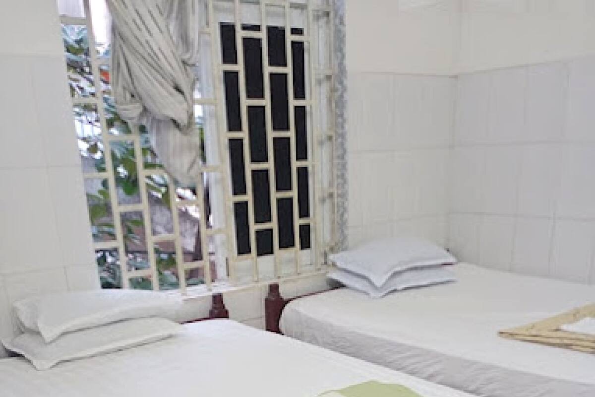Una habitación con dos camas, ropa de cama blanca, una ventana con cortina y vistas a la vegetación.
