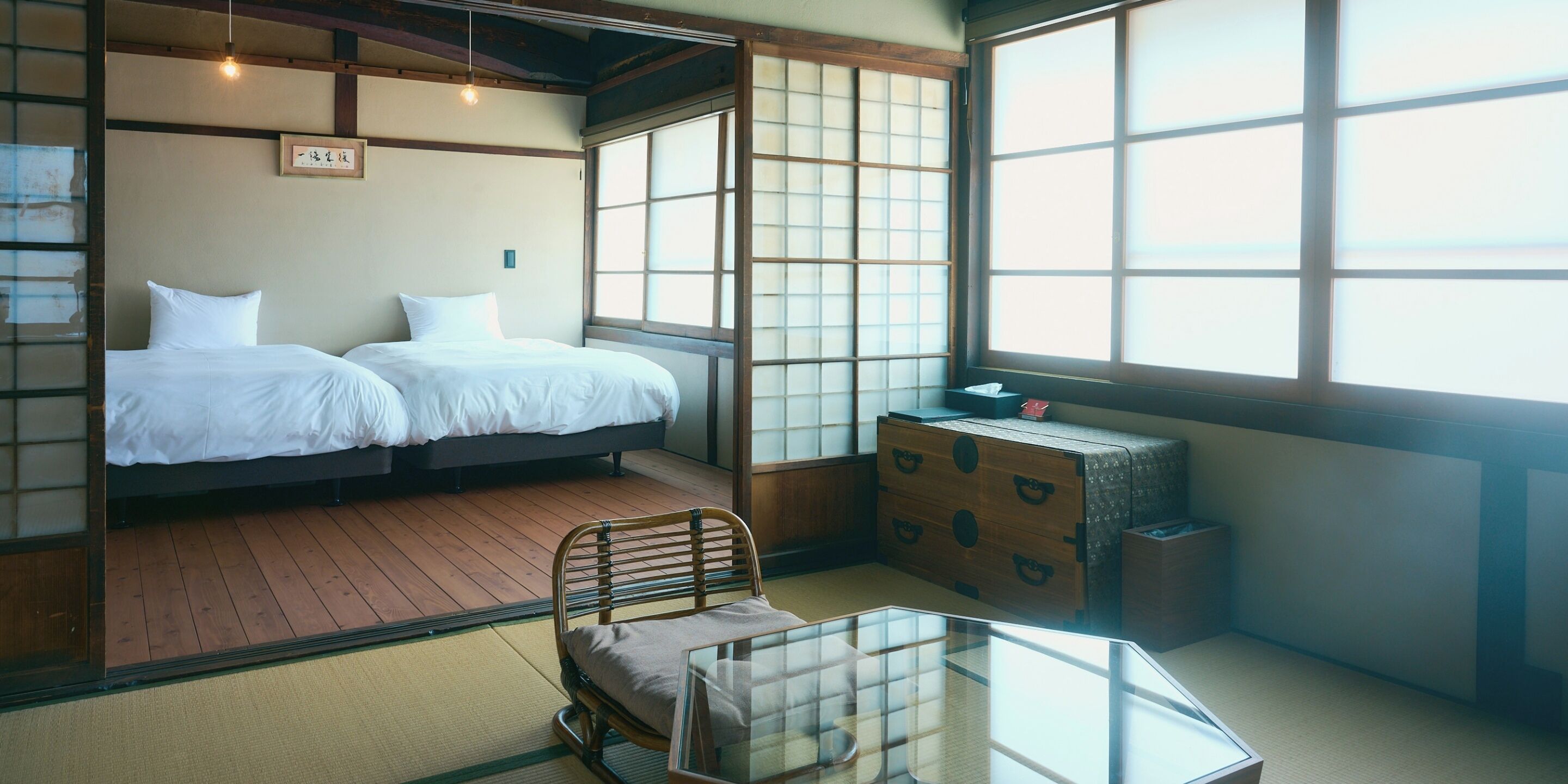 A traditional Japanese room with tatami flooring, a low wooden bed, a small table, and a sliding shoji screen.
