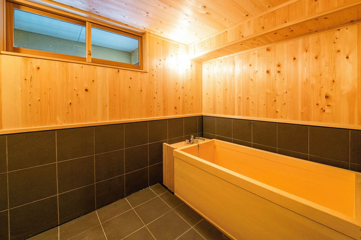 A wooden interior with a bathtub, tiled walls, and a window.