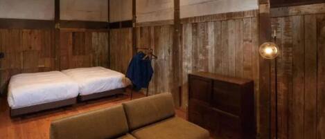 A rustic room with two beds, a sofa, a small table, and a floor lamp.