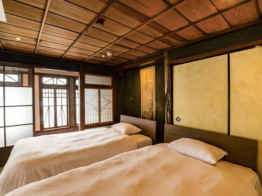 Una habitación tradicional japonesa con dos camas, vigas de madera en el techo, puertas correderas shoji y suelo de esteras tatami.