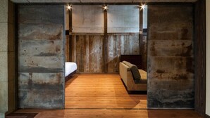 A room with a wooden floor, a bed, a sofa, and a stone wall. - NIPPONIA Chichibu Monzenmachi (Chichibu)