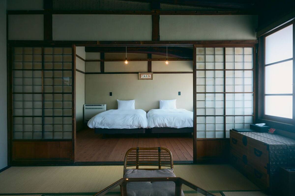 A traditional Japanese-style room with tatami flooring, two beds, a wooden chair, and shoji screens.