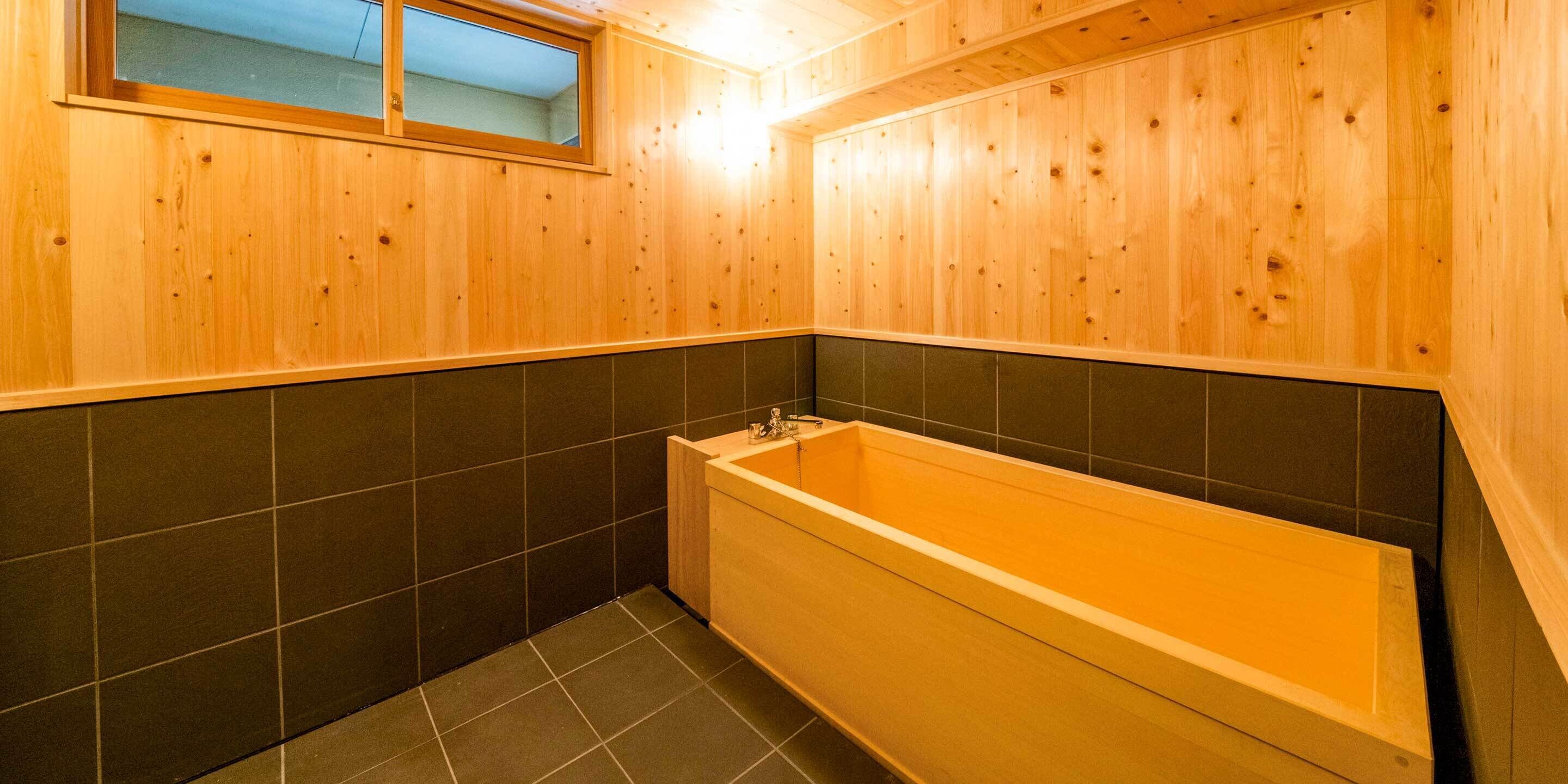 A wooden bathroom with a bathtub, dark tiled walls, and a window.
