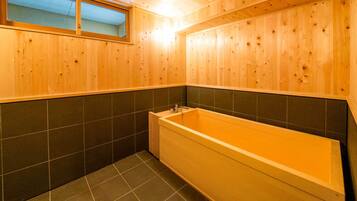 A wooden bathroom with a bathtub, dark tiled walls, and a window.