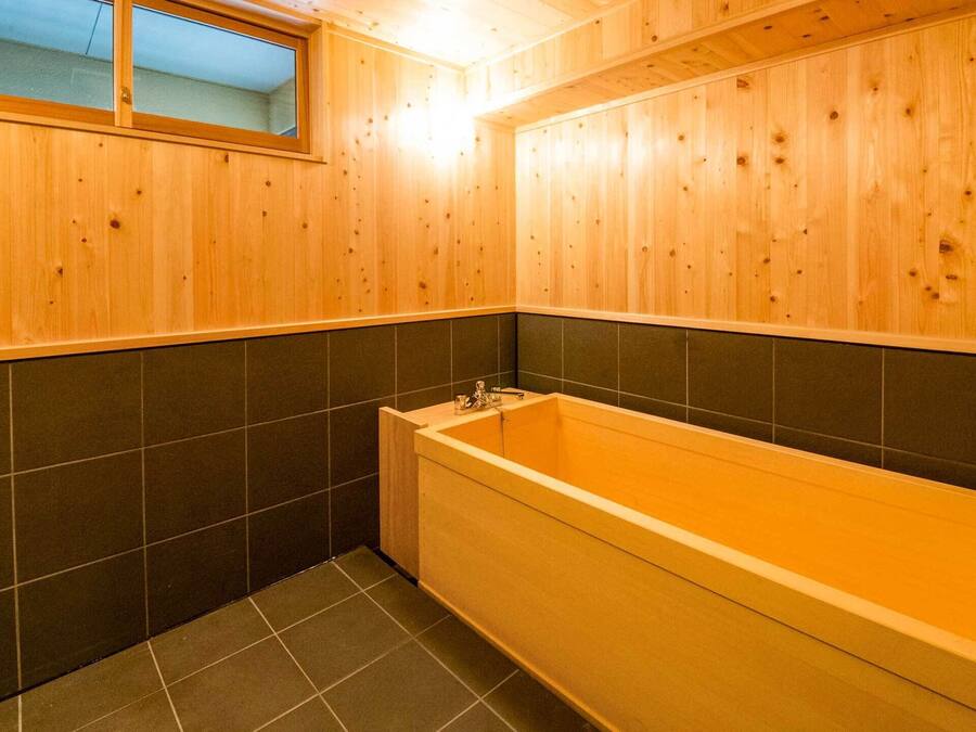 A wooden bathroom with a bathtub, dark tiled walls, and a window.