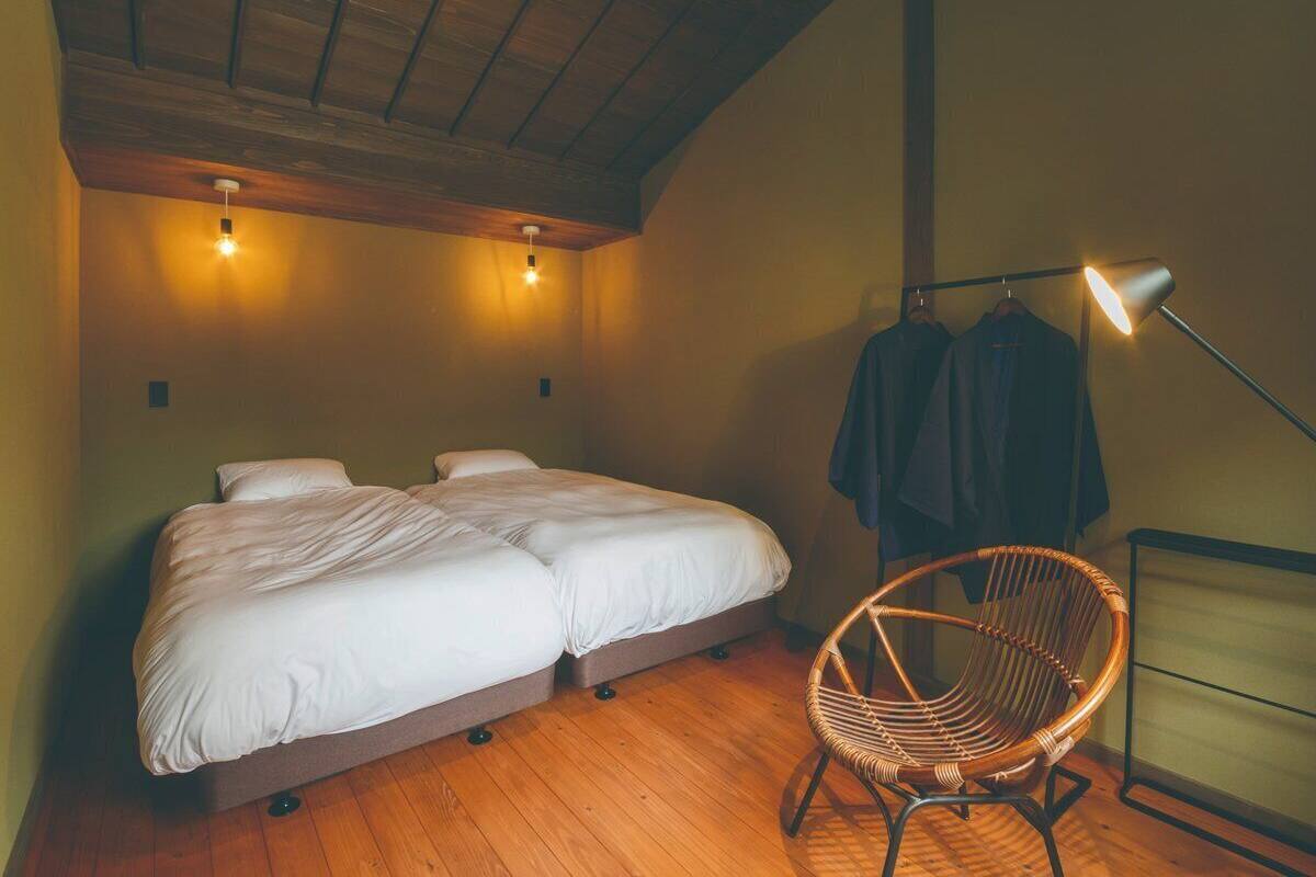 A bedroom with a double bed, a wicker chair, and a hanging clothes rack.