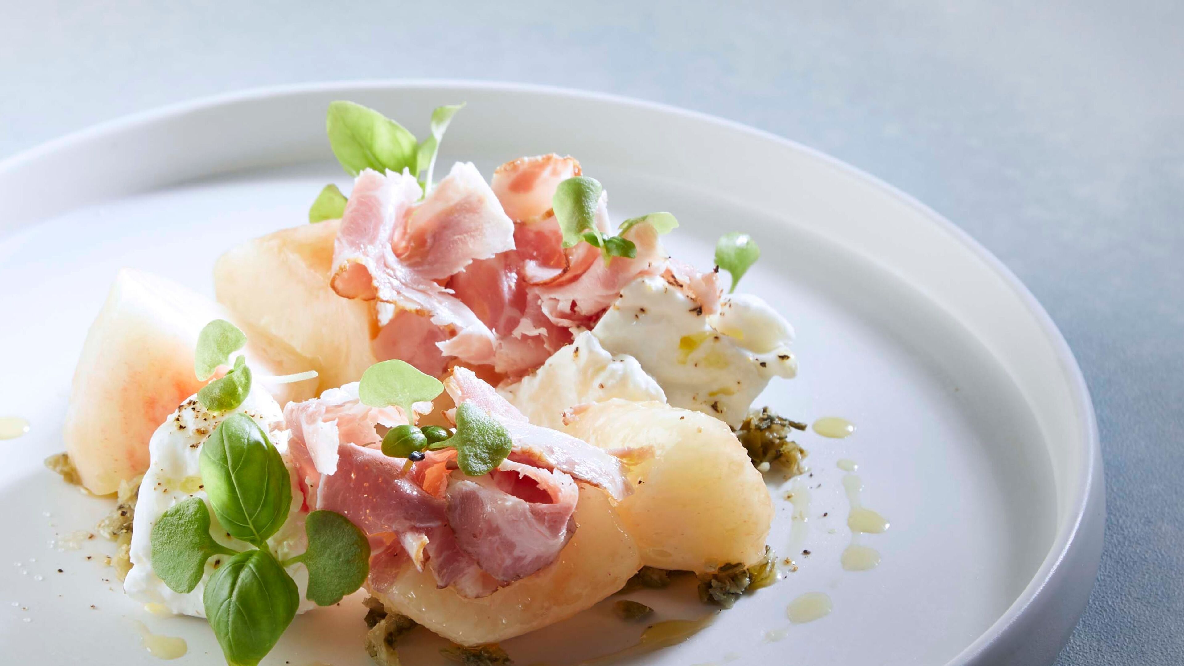A plate of food with potatoes, prosciutto, and greens.
