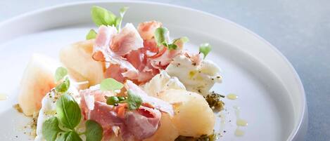 A plate of food with potatoes, prosciutto, and greens.