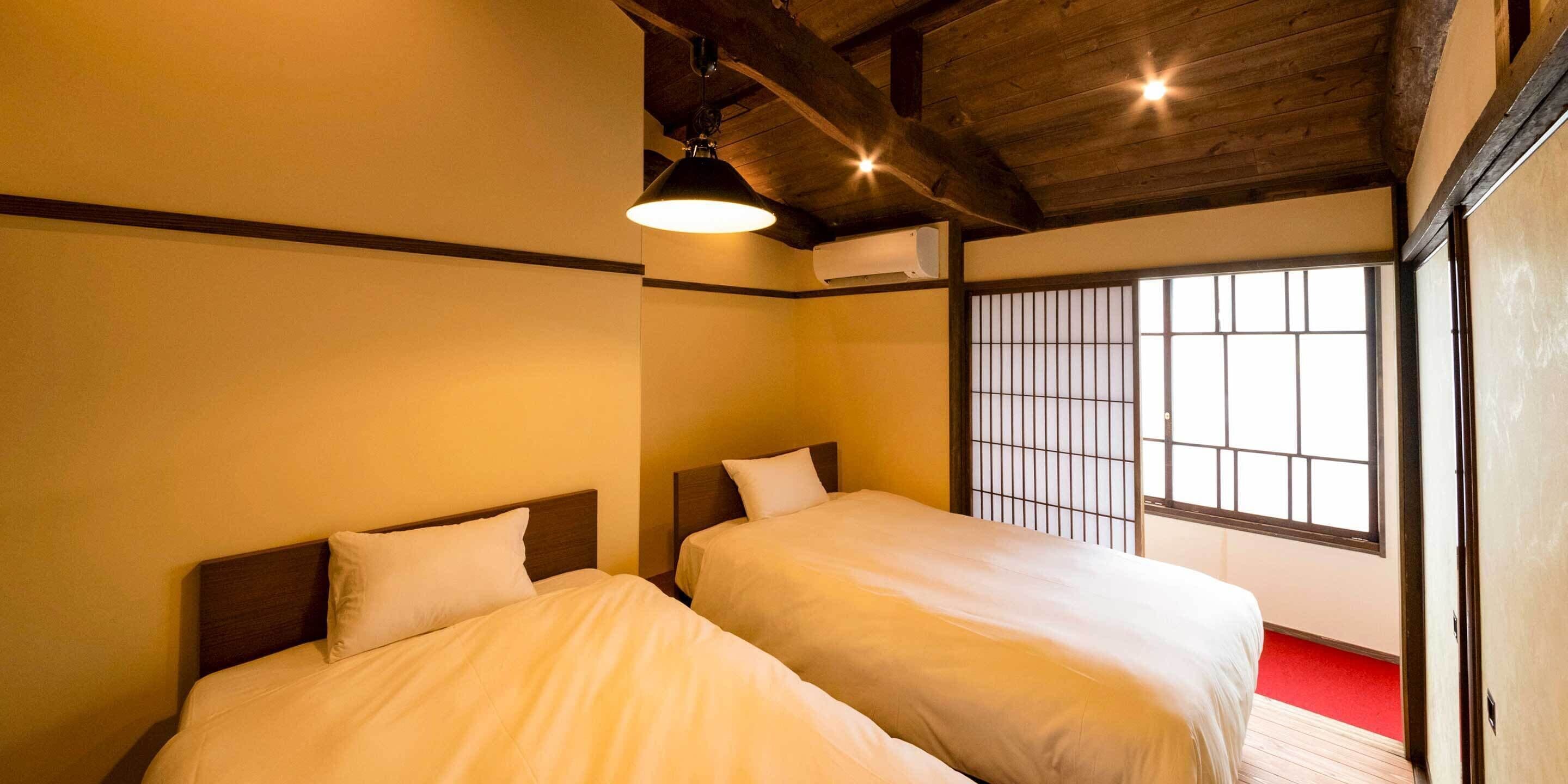 Une chambre d’hôtel avec deux lits, un plafond en bois et une fenêtre avec des barreaux.