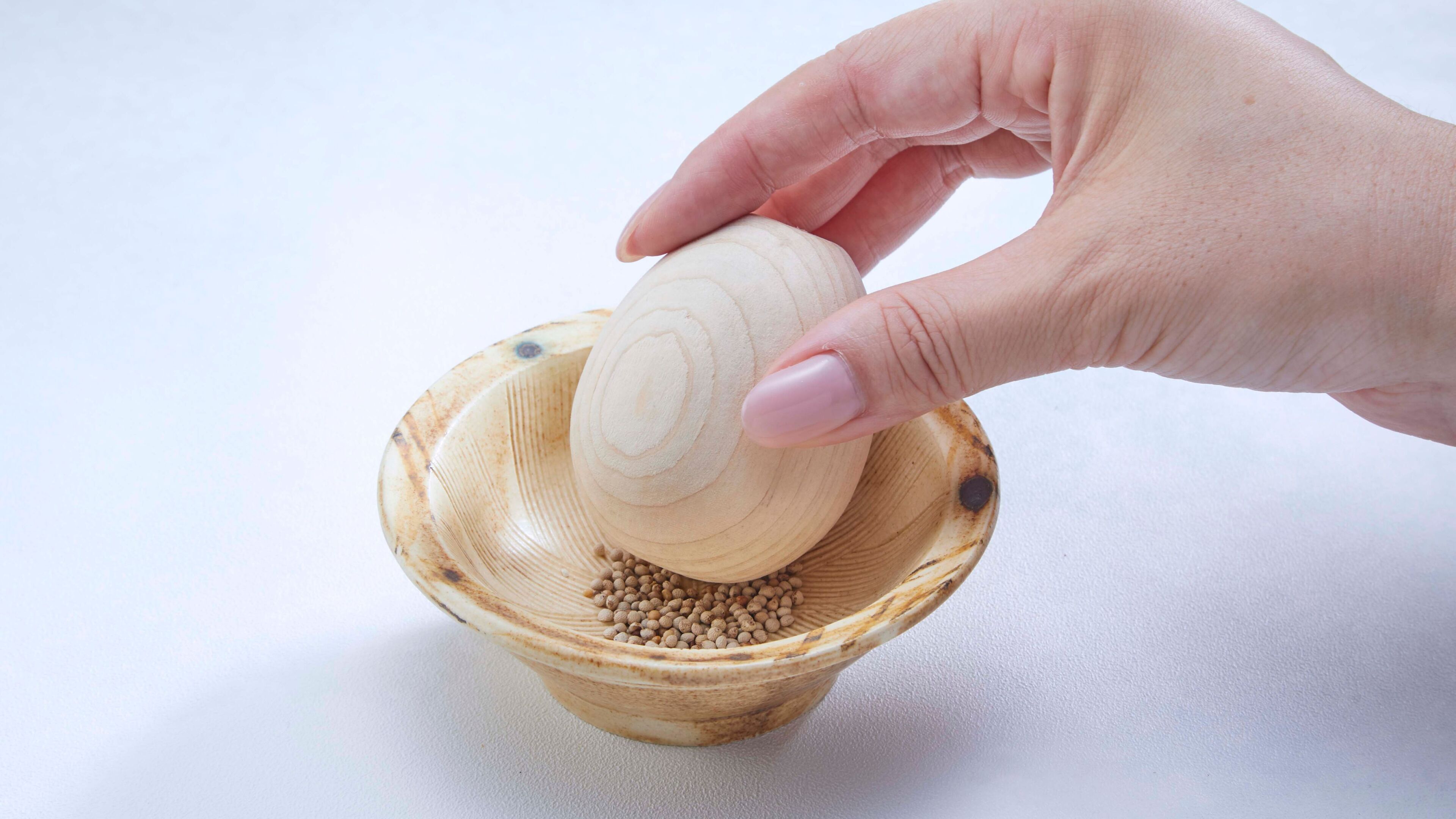 A hand holding a wooden object over a bowl filled with small round items.