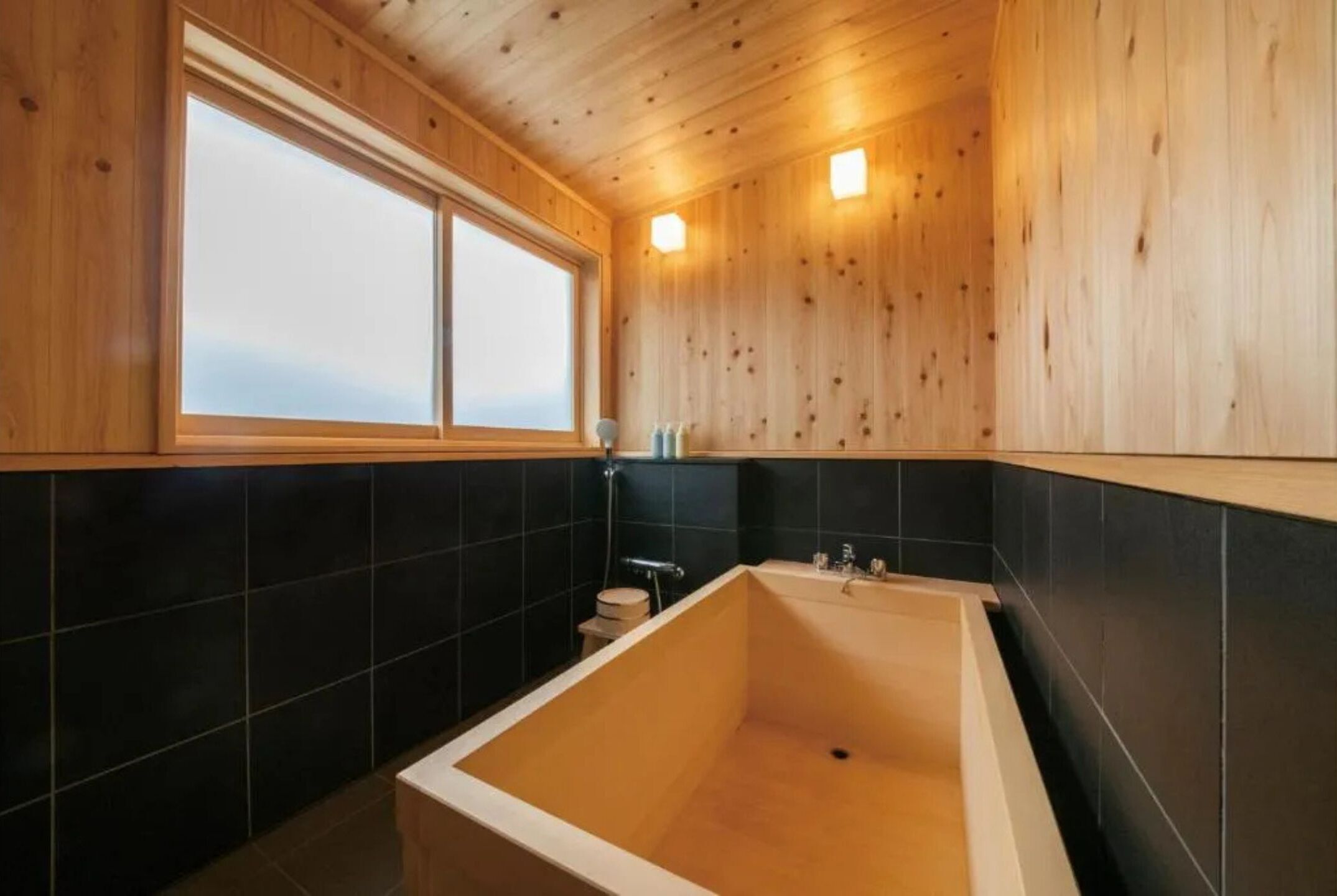 A wooden cabin bathroom with a bathtub, a window, and black tiled walls.