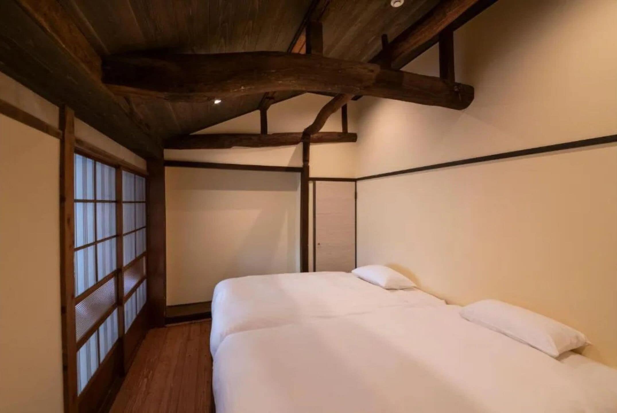 A room with a wooden ceiling, a bed with white bedding, and a sliding door with frosted glass panels.