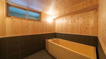 A wooden-paneled bathroom with a bathtub, a window, and dark tiled walls.