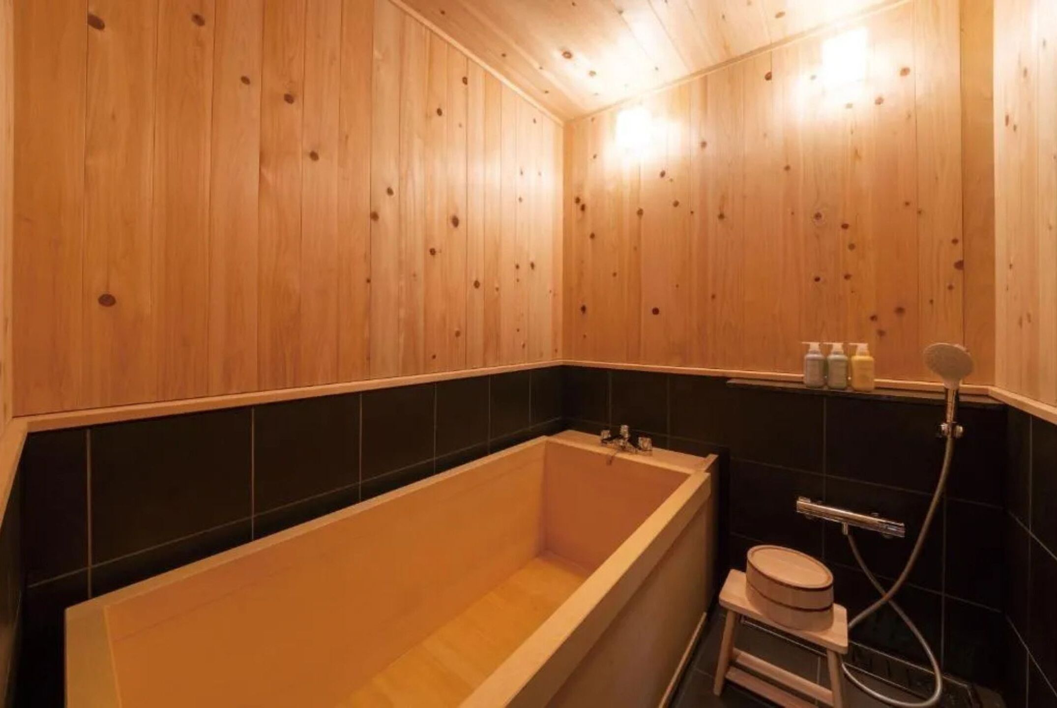 Une salle de bain aux murs lambrissés, équipée d’une baignoire, de toilettes et d’un espace douche.