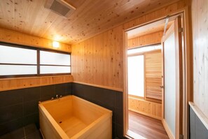 Un intérieur en bois avec une baignoire, une fenêtre avec des stores et une porte donnant sur une autre pièce.