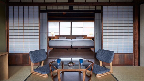 A traditional Japanese room with tatami flooring, two beds, a low table with a teapot, and two chairs. - NIPPONIA Chichibu Monzenmachi (Chichibu)