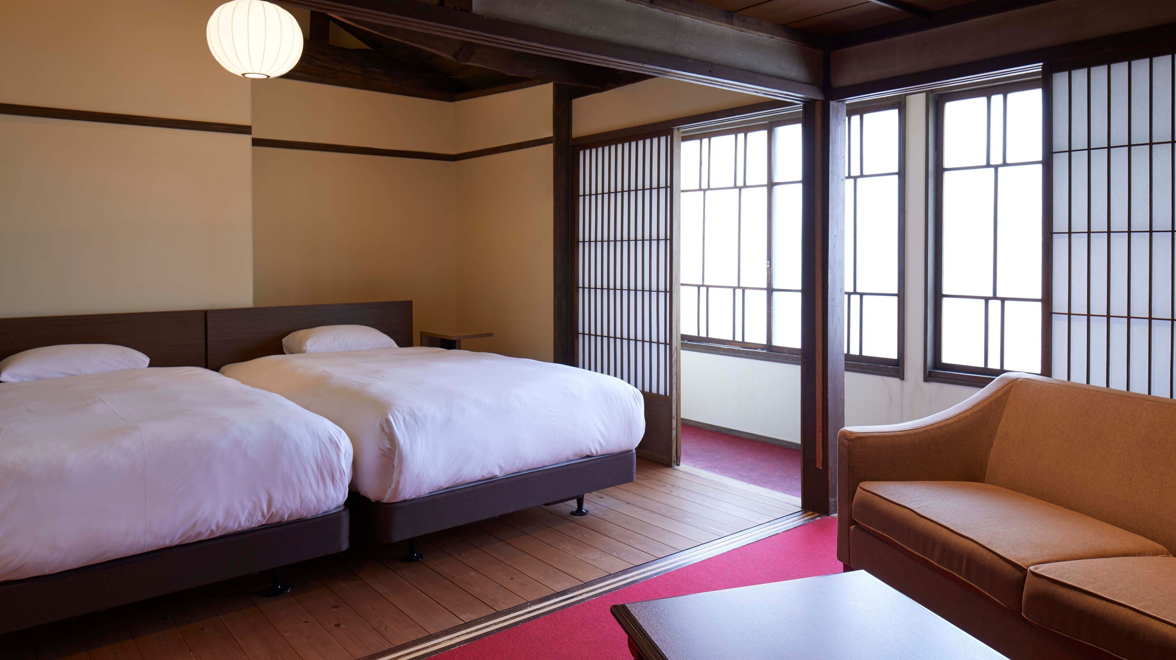 A hotel room with two beds, a sofa, and large windows with traditional wooden frames.