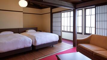 A hotel room with two beds, a sofa, and large windows with traditional wooden frames.
