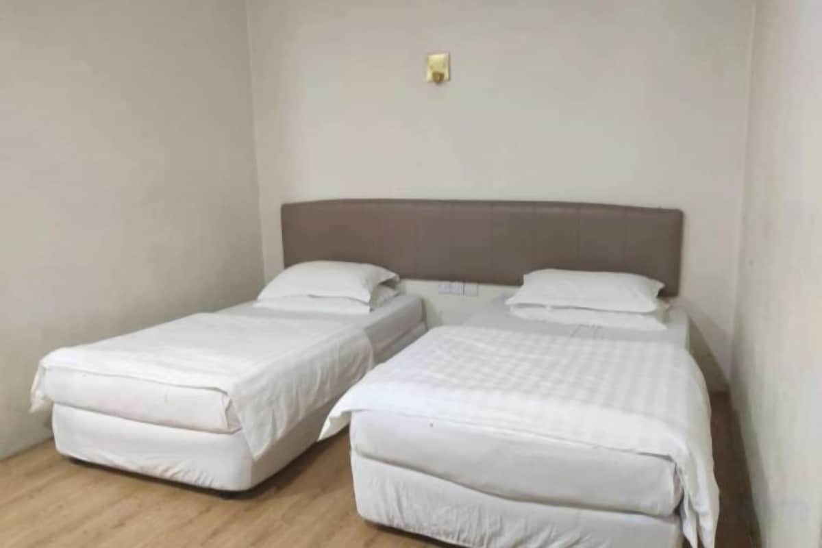 A room with two single beds, a wooden floor, and a plain wall.