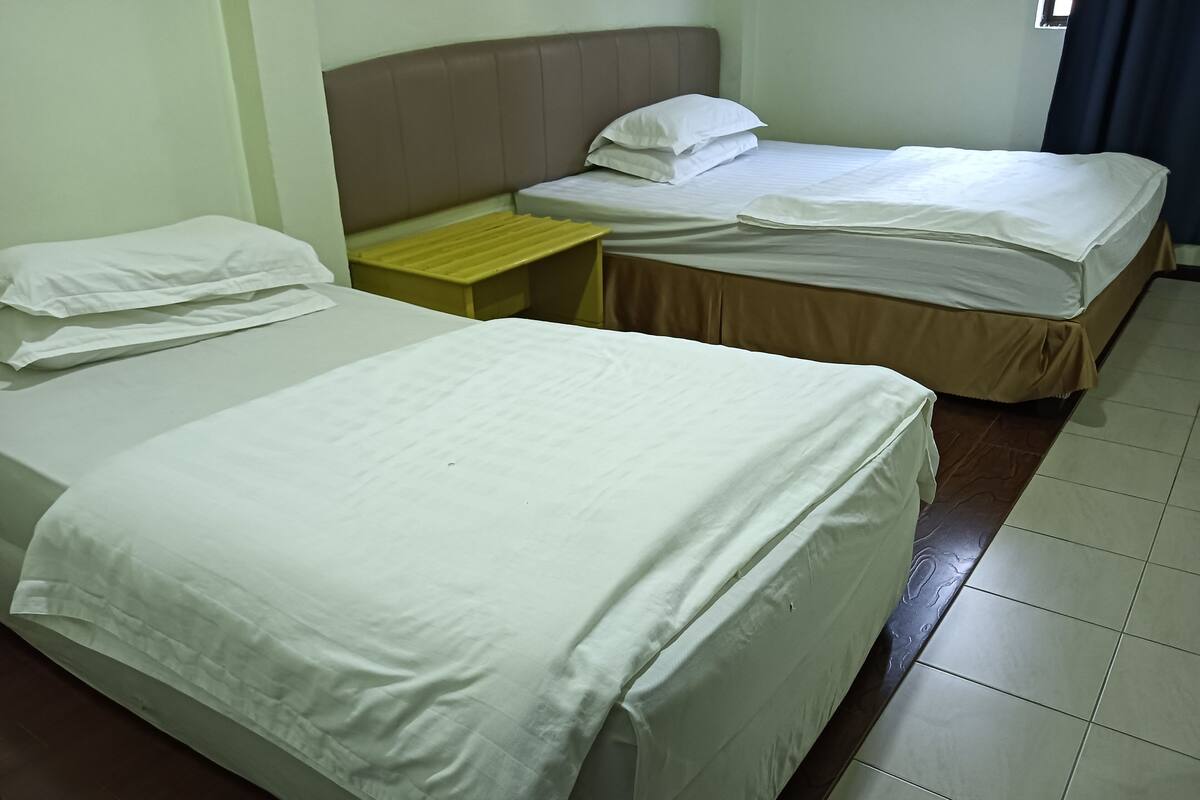 A hotel room with two beds, a wooden nightstand, and a window with curtains.