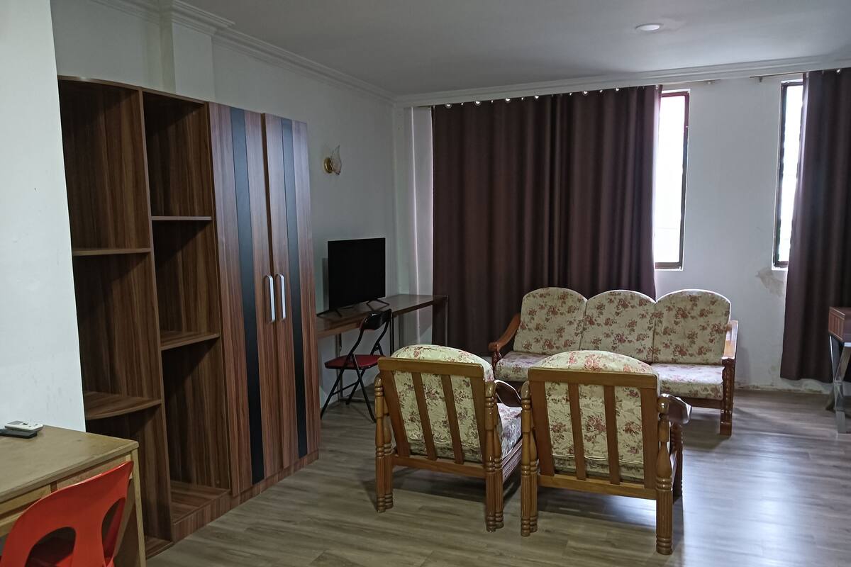 A living room with a wooden cabinet, a television, a sofa, and a red chair.
