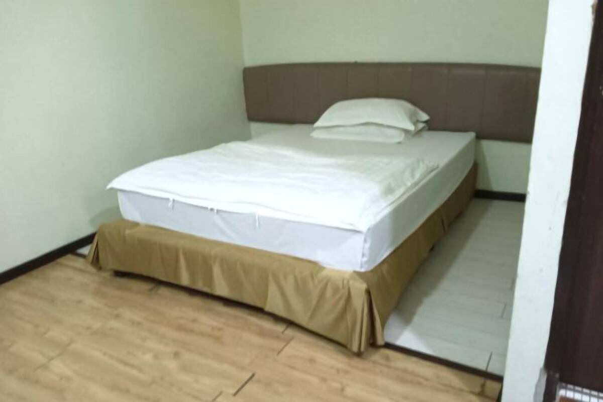 A single bed with a headboard, a brown bed skirt, and a wooden floor.
