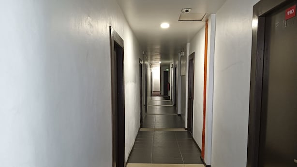 Un pasillo largo y estrecho con puertas a ambos lados, suelo de baldosas y una lámpara en el techo.