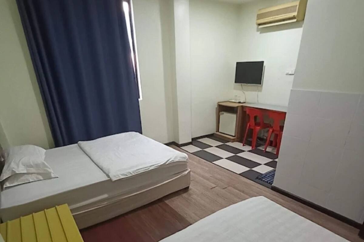 A hotel room with two beds, a small desk, a TV, and a window with curtains.