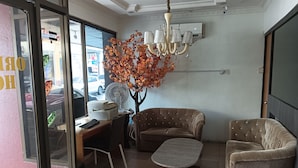 Una habitación con un escritorio, dos sillones, una mesita, un árbol decorativo y una araña.