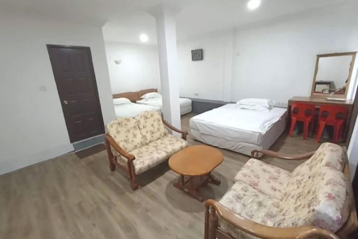 A room with a bed, two sofas, a small table, and a desk with a mirror.