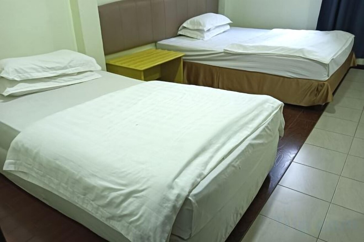 Two beds with white linens, a wooden nightstand, and a plain wall.