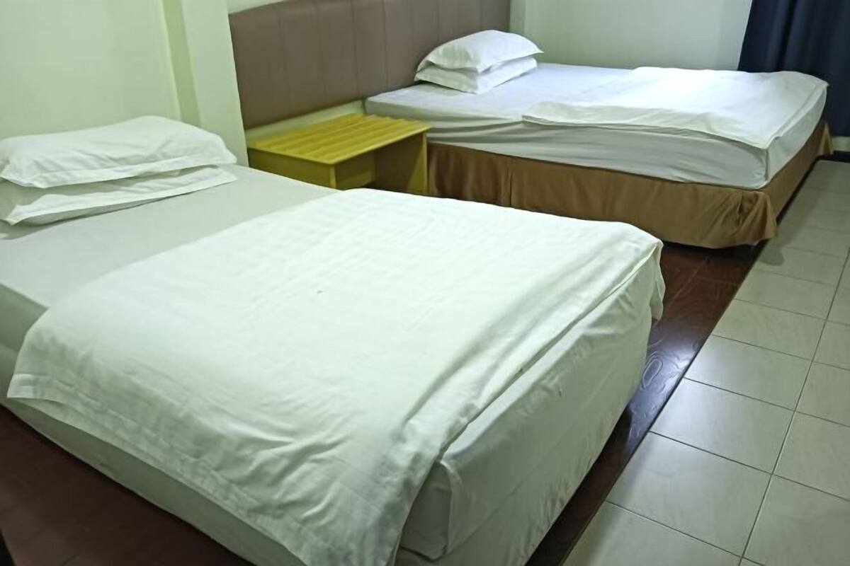 A hotel room with two beds, a small wooden nightstand, and a headboard.
