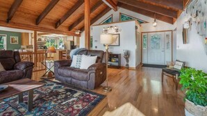 A spacious living room with wooden beams, a leather sofa, a patterned rug, and a dining area with a table and chairs. - Lakeview Mel's Place (Bayview)