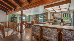 A spacious kitchen with wooden beams, a dining area with patterned chairs, and a bar with stools. - Lakeview Mel's Place (Bayview)