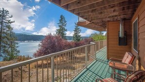 A wooden deck with a view of a lake and mountains, a fireplace, and two striped chairs. - Lakeview Mel's Place (Bayview)