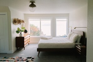 Ein Schlafzimmer mit Bett, Kommode, Fenstern und einer Deckenleuchte.