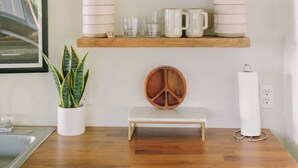 A kitchen with wooden shelves holding various kitchenware, a potted plant, a peace sign decoration, and a white appliance on the counter. - Hilltop Retreat w/ Lake & Mountain Views (Hope)