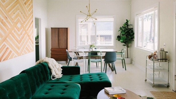 A modern living room with a green sofa, a dining area with a table and chairs, a wooden cabinet, and a large window. - Hilltop Retreat w/ Lake & Mountain Views (Hope)