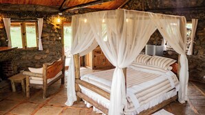 Un dormitorio con paredes de piedra, una cama con dosel, un banco de madera y una pequeña mesa.