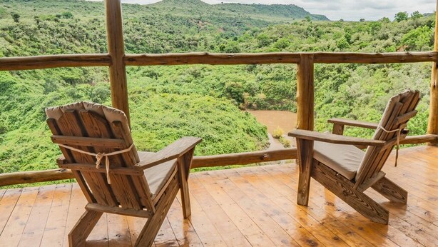 Dos sillas de madera en una terraza de madera con vistas a un paisaje verde exuberante.