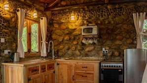 Una cocina rústica con armarios de madera, una pared de piedra, un microondas, una estufa y un lavabo.